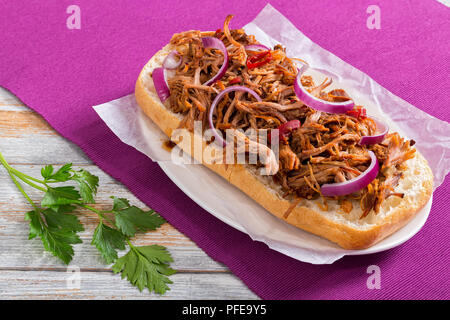 Grill zog Schweinefleisch ciabatta Öffnen pikant Sandwich, rote Zwiebel und Chili auf Pergamentpapier auf dem ovalen Schild auf alte weiße Holztisch mit Petersilie, Stockfoto