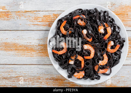 Lecker Tintenfisch Tinte Pasta mit Garnelen auf einem weißen Teller auf alte Holzbohlen, horizontale Ansicht von oben, close-up Stockfoto