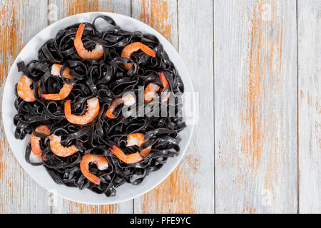 Lecker Tintenfisch Tinte Pasta mit Garnelen auf weiße Platte, auf alten hölzernen weißen peeling Planken, Ansicht von oben Stockfoto