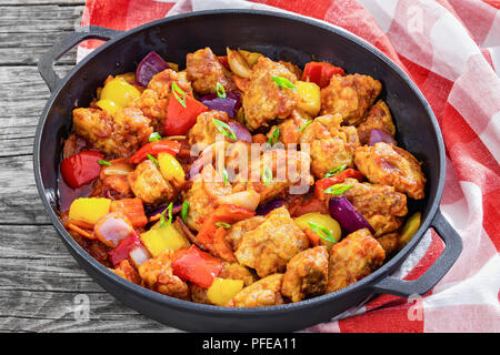 Süß und Sauer gebratenes Schweinefleisch Chunks mit Gemüse, mit grünen Zwiebeln in Eisen stewpan auf dunklem Hintergrund mit Küchentuch sprengte, Tradition Stockfoto