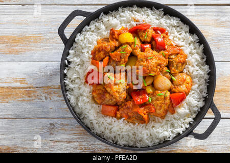 Reis und süß und sauer gebratenes Schweinefleisch Chunks mit Paprika, Zwiebeln, Ananas und Tomatensauce bestreut mit Frühlingszwiebeln in Eisen stewpan auf weißem Plan Stockfoto