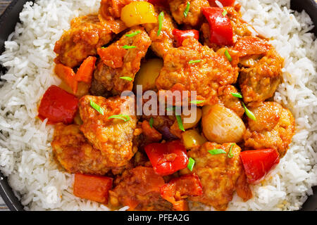 Reis und süß und sauer gebratenes Schweinefleisch Chunks mit Paprika, Zwiebeln, Ananas und Tomatensauce bestreut mit Frühlingszwiebeln in Eisen stewpan auf weißem Plan Stockfoto