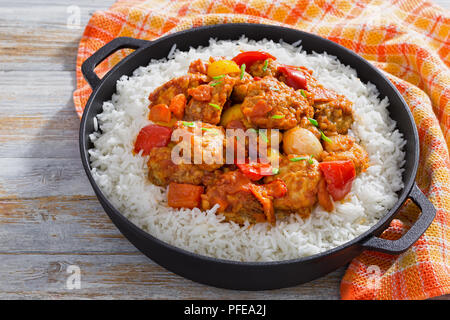 Reis und süß und sauer gebratenes Schweinefleisch Chunks mit Paprika, Zwiebeln, Ananas und Tomatensauce mit Frühlingszwiebeln in Eisen stewpan mit Küche sprengte Stockfoto