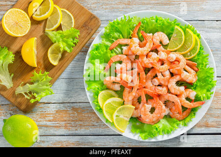 Köstlich frischer Salat mit Garnelen, grüner Salat und Zitronenscheibe auf weißem platter auf alten rustikalen abblätternde Farbe Tabelle, Schneidebrett mit Stücken von Le Stockfoto