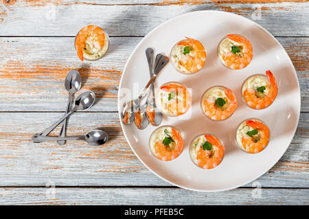 Shot-Glass Garnelen mit Sauce Tartar - einfach Cocktail Rezept für festliche Partei, auf weissem Teller mit Löffel auf alten weißen Holz- Tabelle, Ansicht von oben Stockfoto