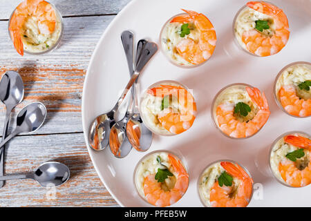 Shot-Glass Garnelen mit Sauce Tartar - einfach Cocktail Rezept für festliche Partei, auf weissem Teller mit Löffel auf alten weißen Holz- Tabelle, Ansicht von oben Stockfoto