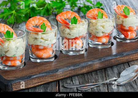 Einzelne Cocktail Shrimps Shot Gläser mit pikanter Sauce Tartar mit Petersilie Blatt auf dunklem Holz Tablett mit Grün dekoriert auf Hintergrund für festliche Stockfoto