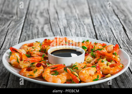 Butter Knoblauch gegrillte Garnelen mit Chili und Petersilie auf weiße Schale mit Sojasauce in kleine Schüssel in der Mitte, auf hölzernen Tisch, Blick f sprengte Stockfoto