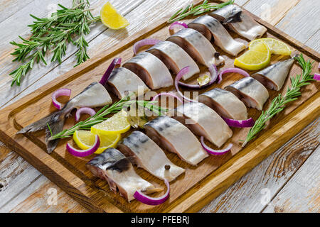 Marinierte Fischfilets frische Makrele Fisch in Scheiben geschnitten mit Rosmarin, Zitrone, roten Zwiebeln und Gewürzen auf Schneidebrett, auf alten Holzbohlen, c Stockfoto