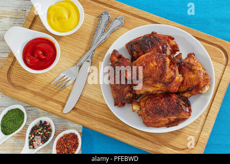 Lecker gebratenes Huhn Oberschenkel, mariniert in Mischung aus Honig, Soja und Austernsauce und Würzmittel auf weißem Schild auf Schneidebrett. Senf und Ketchup. Stockfoto