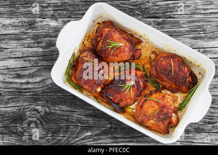 Gegrillte Pouletschenkel mit Rosmarin und Gewürze in rechteckigen braten Teller auf alten weißen Holzbretter, Ansicht von oben Stockfoto