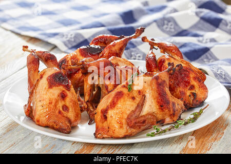 Grill Wachteln mit Thymian auf Teller auf weißen Tisch mit Küchentuch auf hölzernen Hintergrund, Nahaufnahme Stockfoto