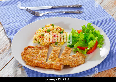 Southern Fried Schweinekoteletts in Stücke geschnitten mit Risotto und frischem Salat und Paprika Salat auf weißen Teller am Tisch mit Messer und Gabel, close-u Stockfoto