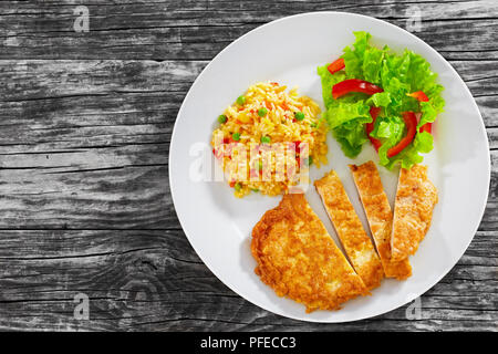 Knusprige Southern Fried Schweinekoteletts in Streifen geschnitten mit herrlich grünen Erbsen. Mais. Karotte Zwiebel würzigen Risotto und frischen grünen Salat auf weiße Platte Stockfoto