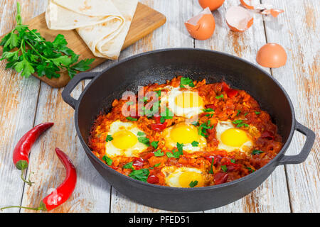 Köstliche Naher Osten grundlegende Shakshuka - gebratene Eier, Zwiebel, Paprika, Tomaten, Paprika und Gewürzen in gusseisernen Pfanne auf alten Holz- Hintergrund mit Sie Stockfoto