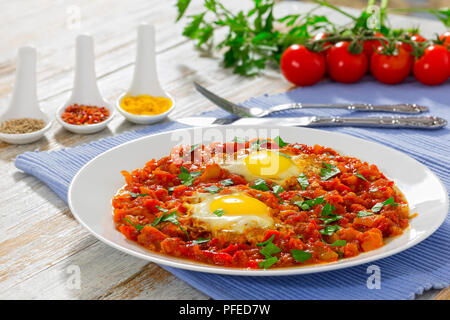 Spiegeleier mit Gemüse bestreut mit Petersilie oder Shakshuka - Paprika, Chili, Tomaten auf weißem Teller am Tisch mat. Gewürze, Cherry tomat Stockfoto