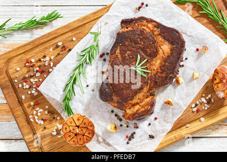 Perfekte Beef Rib-eye Fleisch saftige Steak gebraten in eiserne Pfanne mit Rosmarin, Olivenöl, Knoblauch, Nelken und Pfeffer, Nahaufnahme, Ansicht von oben Stockfoto