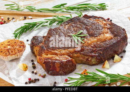 Leckere heiße Beef ribeye Fleisch saftige Steak gebraten in eiserne Pfanne mit Rosmarin, Olivenöl, Knoblauchzehen, Butter, Pfeffer, Nahaufnahme, Ansicht von oben Stockfoto