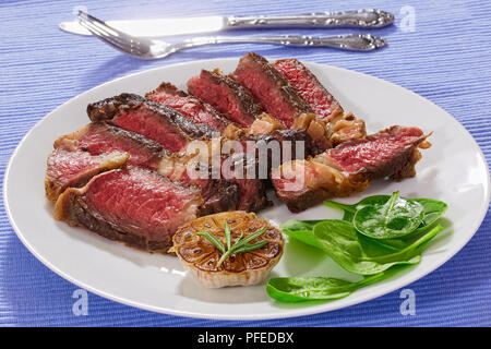 Hot Beef Rib-eye Fleisch saftige Steak, Medium, in Scheiben auf Weiß Schüssel Salat mit Spinat und Knoblauch geschnitten, Nahaufnahme, Ansicht von oben Stockfoto