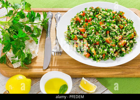 Petersilie, Minze, Tomate, Salat oder Tabbouleh auf weißem platter auf Schneidebrett mit grunchy Fladenbrot, einfache und gesunde vegetarische Gericht, Olivenöl und Stockfoto