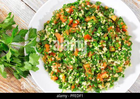 Bulgur weizen Glutenfrei vegetarisch Petersilie, Minze, Frühlingszwiebeln, Tomatensalat, beträufelt mit Zitronensaft und Olivenöl auf weißem Teller auf abblätternde Farbe t Stockfoto