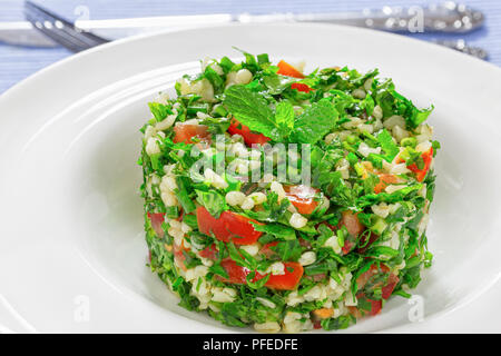 Tabbouleh oder Petersilie, Pfefferminz, Frühlingszwiebeln, Tomatensalat, beträufelt mit Zitronensaft und Olivenöl, mit Minze auf weißem Teller dekoriert, in der Nähe Stockfoto
