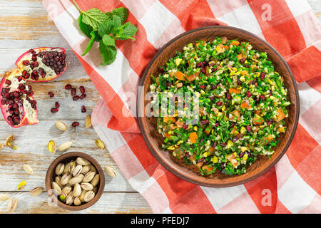 Köstliche tabbouleh Salat mit Granatapfel, Pistazien, Petersilie, Pfefferminze, Frühlingszwiebeln, Tomaten auf Lehm Teller auf Tischdecke, mediterranen Cuisi Stockfoto