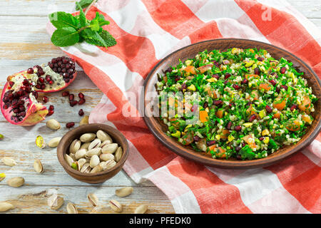 Lecker Salat mit Granatapfel, Pistazien, Petersilie, Pfefferminze, Frühlingszwiebeln, Tomaten auf Lehm Teller auf Tischdecke, mediterrane Küche, Schließen - Stockfoto