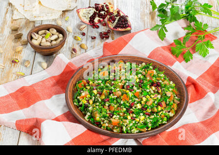 Tabbouleh Salat mit Granatapfel, Pistazien, Petersilie, Pfefferminze, Frühlingszwiebeln, Tomaten auf Lehm Teller auf Tischdecke, mediterrane Küche, Schließen - Stockfoto
