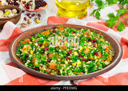 Tabbouleh Salat mit Granatapfel, Pistazien, fein gehackte Petersilie, Pfefferminz, Frühlingszwiebeln, Tomaten auf Lehm Teller auf Tischdecke, Mittelmeer Stockfoto