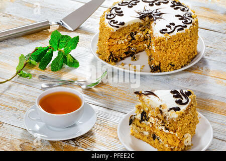 Köstliche Teil der Schwamm prune Kuchen mit glatte, glänzende Glasur Schokolade dekoriert, in Scheiben schneiden, auf alten, dunklen Holzbohlen mit Tasse schwarzen Kaffee, Ca Stockfoto