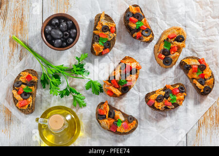 Tapas gekrönt mit Fischfilet in Tomatensauce geschmorte, olive Ringe und roten Paprika, auf weißem Papier mit Speiseöl und Schüssel von schwarz Oli Stockfoto