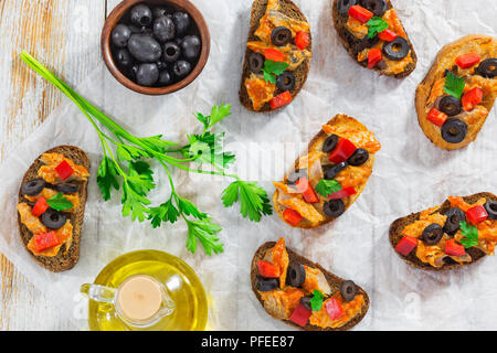 Bruschetta mit Fischfilet, Olivenöl, Ringe und roten Paprika, auf weißem Papier mit Speiseöl und Schüssel von schwarzen Oliven auf Holz- Tabelle, Ansicht Stockfoto