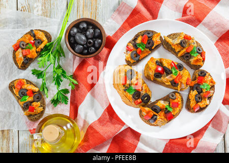 Bruschetta mit Stücken von Fisch gedünstet in Tomatensoße, Ringe von schwarzen Oliven, rote Paprika auf weiße Platte auf Küche Tuch, Ansicht von oben Stockfoto