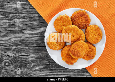 Saftige leckere panierte Fleisch Schnitzel auf weißem Teller auf alten, dunklen Holzbrettern, Ansicht von oben Stockfoto