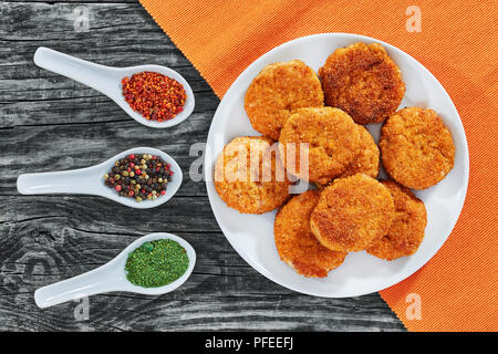 Saftig lecker beschichtet mit Semmelbröseln und dann gebraten Hähnchen Schnitzel auf weissem Teller mit Gewürzen in Porzellan Löffel auf alten, dunklen Holzbrettern, Anzeigen Stockfoto