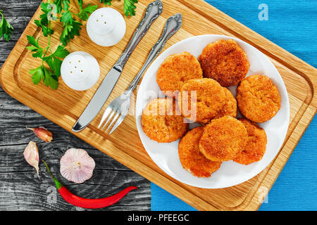 Saftige chicken Schnitzel auf weissem Teller mit Salz- und Pfefferstreuer, Petersilie auf Holz Schneidebrett, Knoblauch und Chili auf alten rustikalen Tisch, vi Stockfoto