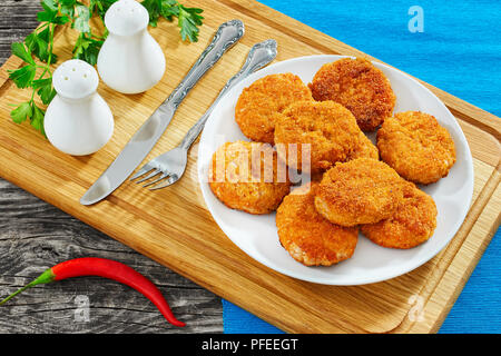 Saftig lecker Huhn, Schwein, Rind Schnitzel auf weissem Teller mit Salz- und Pfefferstreuer, Petersilie auf Schneidebrett, Chili auf alten Holztisch paniert, Stockfoto