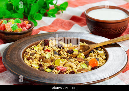 Müsli mit Honig, Haferflocken, Cashewnuss, Mandeln, Pistazien, Rosinen und getrockneten Cranberry in Ton Platte auf Küchentuch mit kandierten Früchten und Schüssel mit Stockfoto