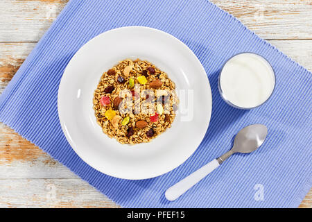 Gesundes Frühstück - Bio Müsli mit Honig, Haferflocken, Cashewnuss, Mandeln, Pistazien, Rosinen und getrockneten Cranberry in weiße Platte mit einem Glas Milch ein Stockfoto