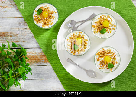 Gesundes Frühstück - frisches Joghurt mit Müsli mit Cocktailkirsche und Minze im Glas Tassen auf weiße Schale mit Löffel dekoriert, Ansicht von Abo Stockfoto