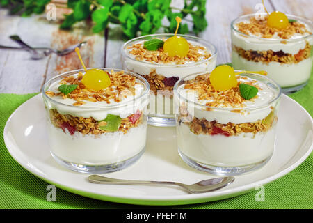 Gesundes Frühstück - Teile der frischen Joghurt mit Müsli und Cocktailkirsche und Minze im Glas Tassen auf weiße Schale mit Löffel, Ansicht von ab Stockfoto