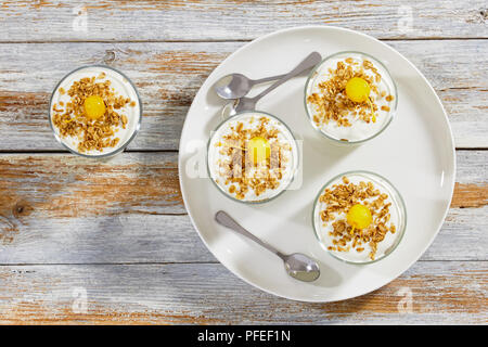 Griechischer Joghurt mit Müsli mit Cocktailkirsche in Glas Tassen auf weiße Schale mit Löffel dekoriert, Ansicht von oben Stockfoto