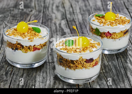 Leckeres Müsli mit Honig, Haferflocken, Pistazien, Rosinen und getrockneten Cranberry in Teil Gläser, dekoriert mit süßen Cocktail-kirsche und Minze auf dunklen Stockfoto