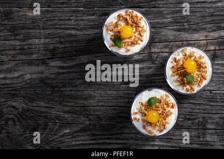 Gesundes Frühstück - Portionen Müsli mit Cocktailkirsche und Minze im Glas Tassen auf dunklen Holztisch eingerichtet, Ansicht von oben Stockfoto
