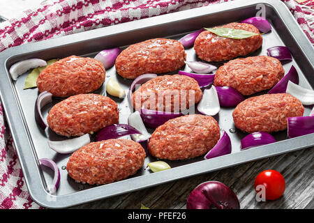 Frischem Boden rohes Fleisch Koteletts mit roten Zwiebeln, Knoblauch und Lorbeer beträufelt mit Olivenöl in Auflaufform mit Küchentuch, Ansicht von oben, Schließen - Stockfoto