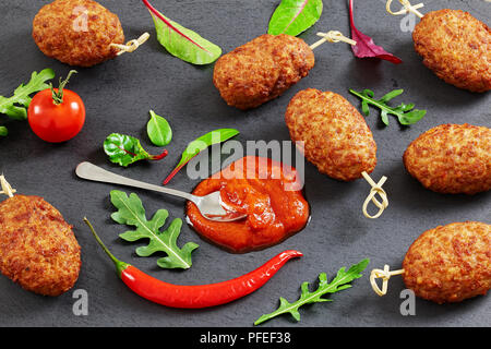 Fleisch schnitzel Kebab gebraten auf Bambus Spieße auf schiefer Platte mit Tomatensoße, Chili Peppers und Salatblättern, close-up Stockfoto