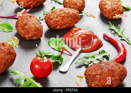 Saftige schmackhaftes Fleisch Schnitzel gebraten auf Bambus Spieße auf schiefer Platte mit Tomatensoße, Chili Peppers und Salatblättern, Ansicht von oben, close-up Stockfoto