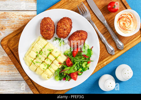 Leckere Kartoffelpüree bestreut mit grünen, saftigen Fleisch Koteletts und frischen gesunden Salat mit Rucola, Sellerie, Salatblätter und Tomaten auf Weiß Stockfoto