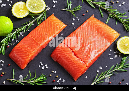 Gesalzene Lachsfilet mit frischem Rosmarin, Salz, Pfeffer und Zitronensaft mischen von Schichten auf schiefer Platte, close-up Stockfoto